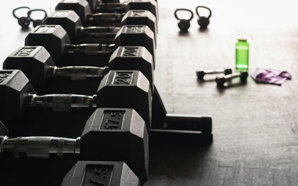A row of black hex dumbbells with small training accessories nearby; illustrative stock photo