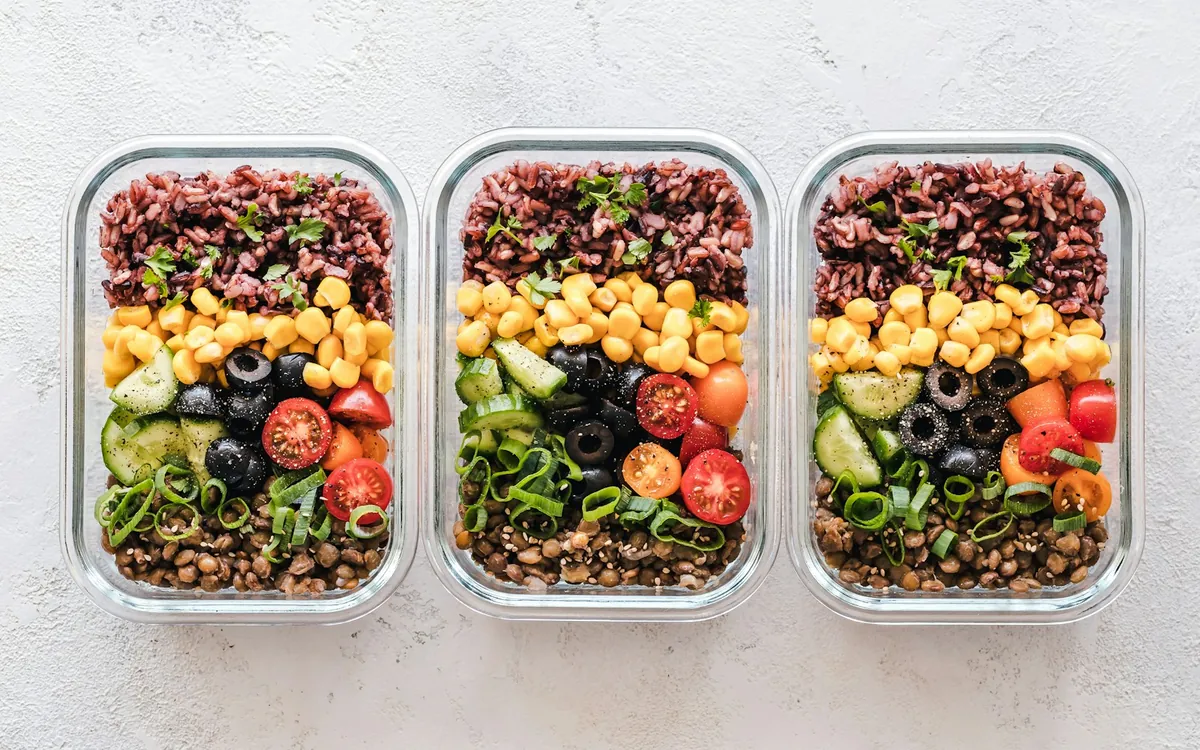 Three food containers filled with grains, lentils, and vegetables; illustrative stock photo