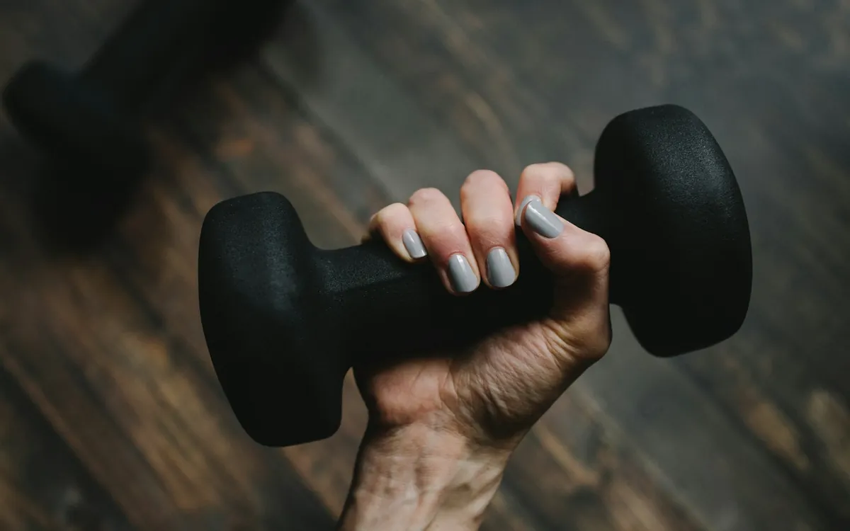 A hand holding a small black dumbbell; illustrative stock photo
