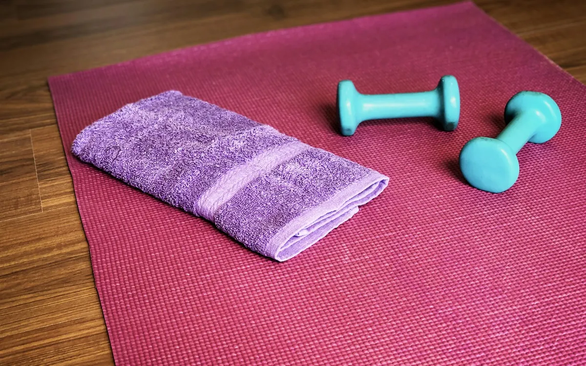 A towel and two light dumbbells arranged on an exercise mat; illustrative stock photo