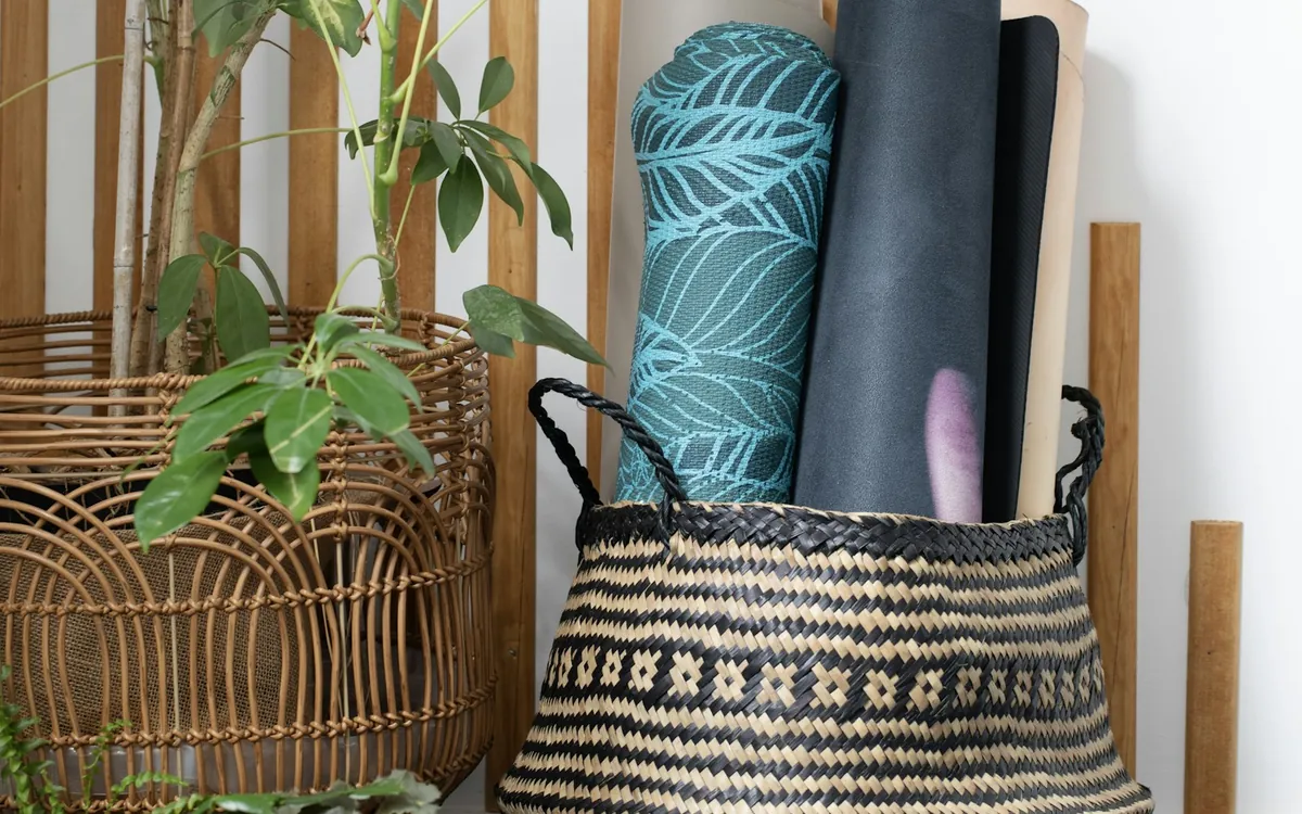 Rolled exercise mats stored in a woven basket beside a plant; illustrative stock photo